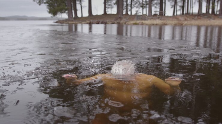 Slomo shot of a man in his late 50s dipping his head under the icy lakewater