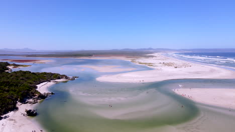 Aerial-riser-reveals-beachgoers-swimming-in-clear-water-of-Klein-River-lagoon