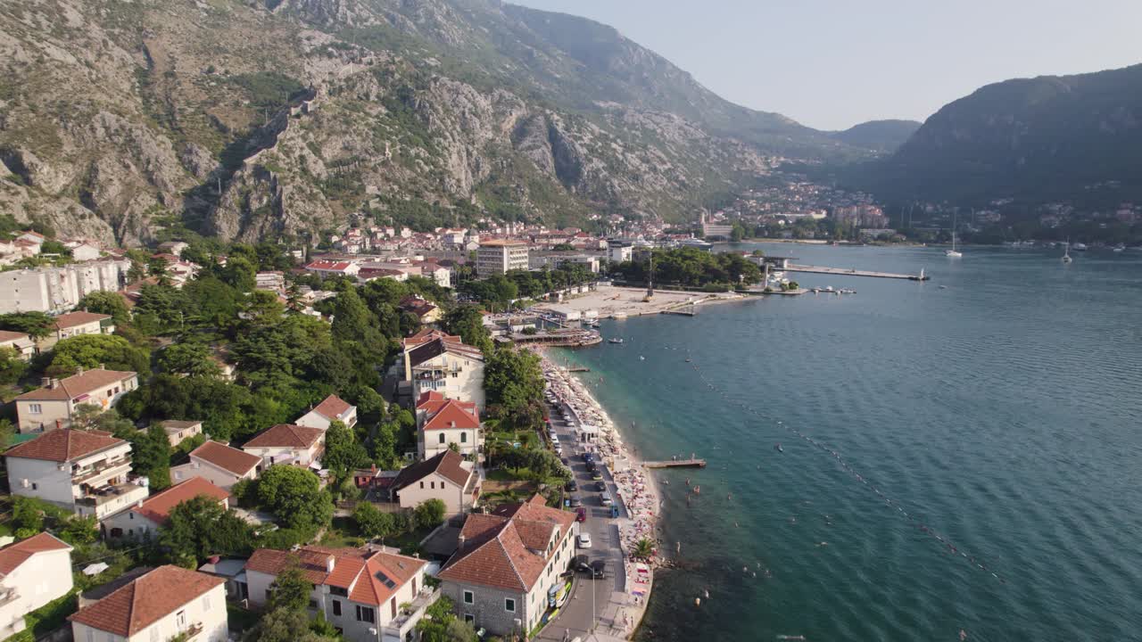 Beach in tourist town Kotor in Montenegro, mountains in the background, aerial flyover