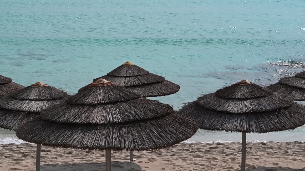 Straw beach umbrellas on the sand facing the turquoise Mediterranean Sea on the coast of Limassol, Cyprus