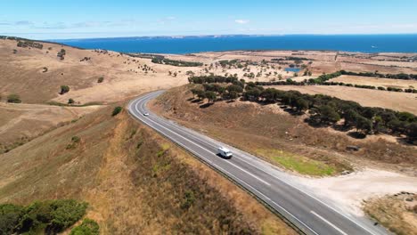 Drohnenaufnahmen,-Die-Rückwärts-Fliegen,-Während-Ein-Wohnmobil-Und-Ein-Auto-Entlang-Einer-Straße-Fahren,-Die-Von-Atemberaubender-Natur-Und-Landschaft-Auf-Der-Fleurieu-Halbinsel-In-Südaustralien-Umgeben-Ist