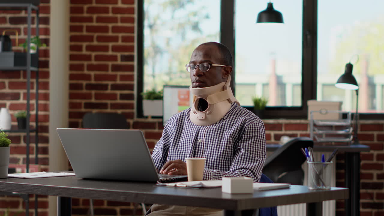 Businessman with medical neck collar working on laptop
