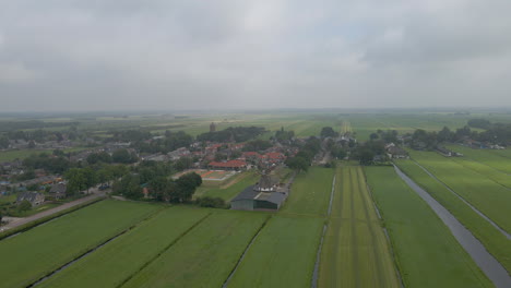 Wide-jib-down-of-a-old,-classic-windmill-with-a-small-Dutch-town-in-the-background