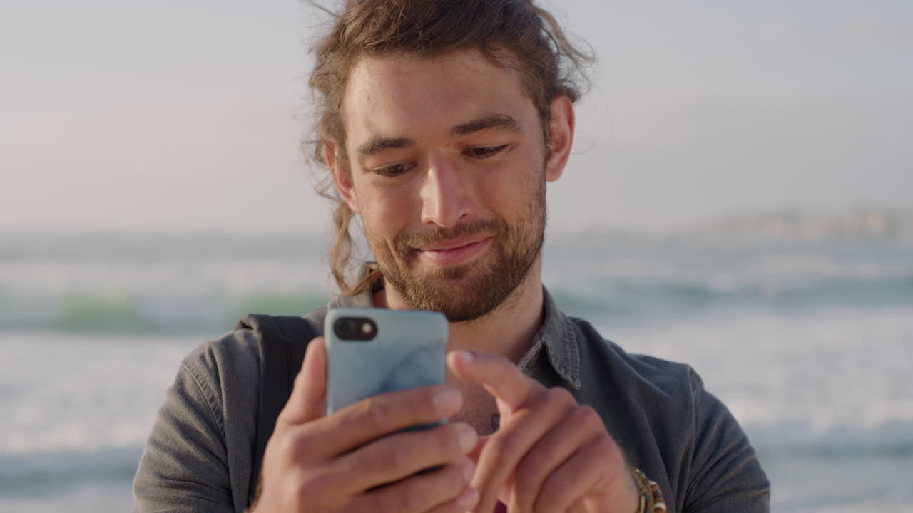 ritratto di un giovane che utilizza uno smartphone, invia messaggi, naviga online, condivide esperienze di vacanza sui social media, gode della comunicazione mobile sullo sfondo di una spiaggia soleggiata