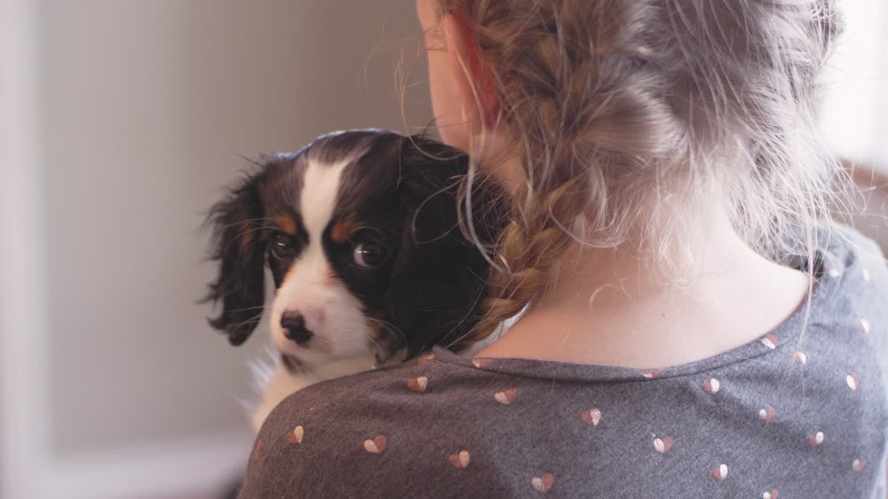 거실에서 사랑스러운 강아지를 들고 있는 어린 소녀의 어깨