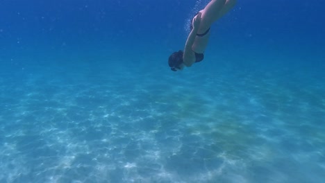 Underwater-scene-under-seawater-surface-of-adult-woman-with-black-bikini-diving-in-crystal-clear-deep-blue-ocean-water-with-mask