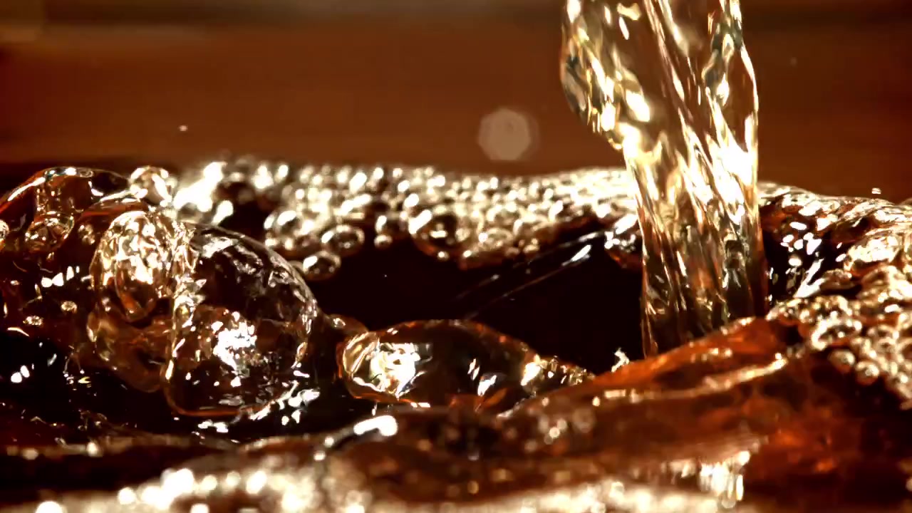 Versamento al rallentatore di liquido dorato che crea bollicine e schizzi