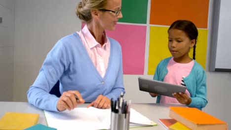 schoolgirl and teacher using digital tablet in classroom