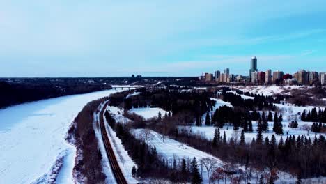 aerial-winter-flyover-Victoria-Park-Ice-Skating-track-rink-by-the-forest-next-to-snow-covered-North-Saskatchewan-River-with-the-Pearl-condominium-skylline-stunning-blue-sky-partly-cloudy-horizon-2-2