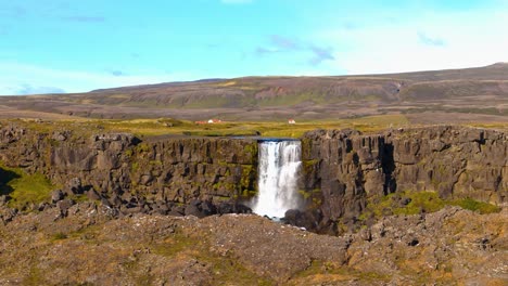 drone aéreo disparado sobre una gran llanura islandesa con una gran cascada que fluye a través de una falla en tierra, clima soleado y cielo azul