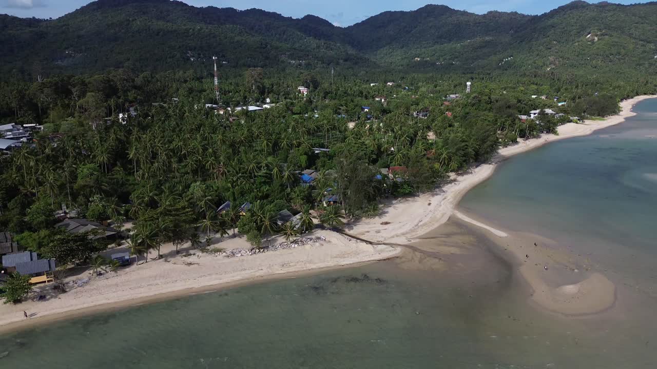Editorial aerial drone footage of Baan Tai Beach on Koh Phangan island, Surat Thani, Thailand, showing tropical palm trees, seaside bungalows, sandy shoreline, and turquoise ocean water