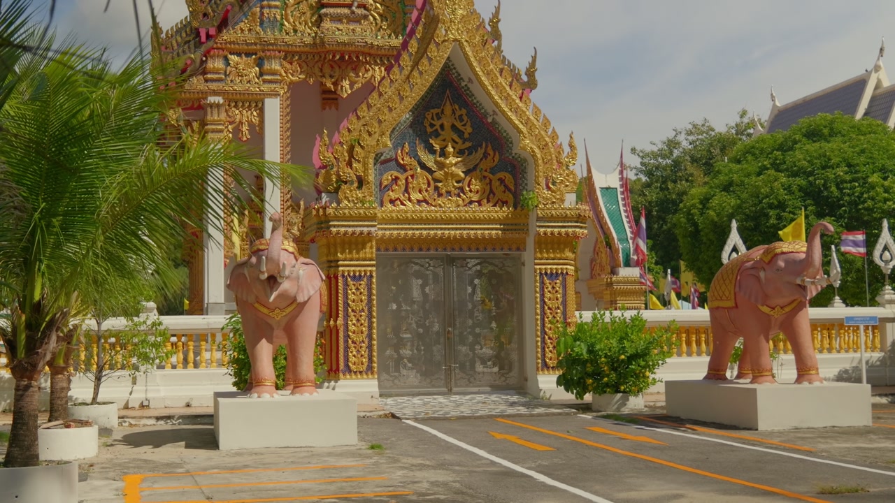 Wide cinematic shot of the ornate golden entrance to Wat Nai Harn temple in Phuket, Thailand. Features iconic pink elephant statues and traditional Buddhist architecture. 4K travel footage.