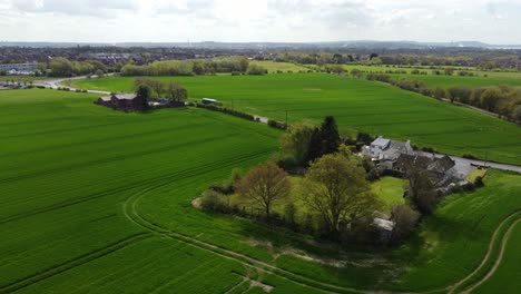 Rural-British-farmhouse-aerial-view-surrounded-by-lush-green-trees-and-agricultural-farmland-countryside-landscape