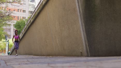 African-american-woman-wearing-earphones-running-in-the-sidewalk