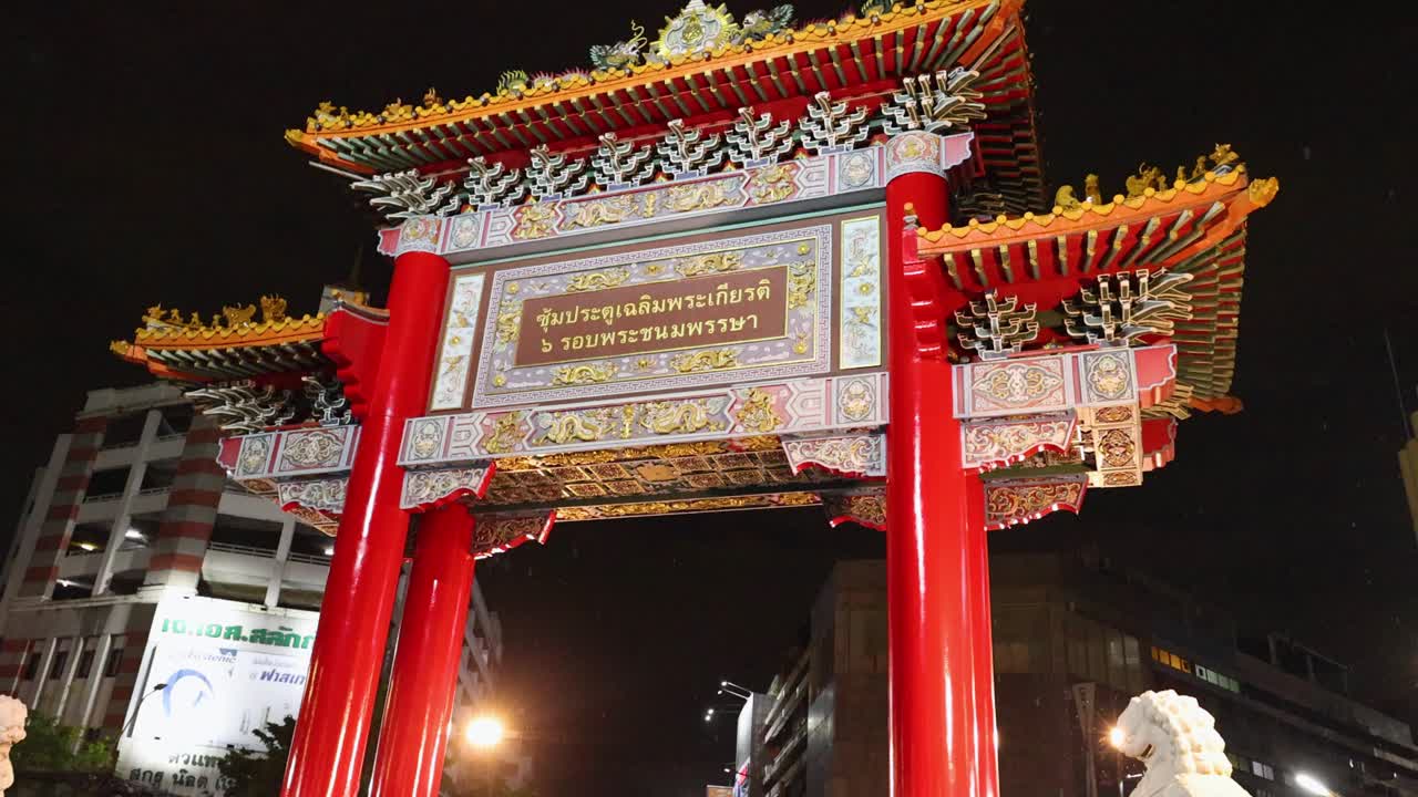 Camera tilts upward on ornate Chinatown archway at night, wet ground reflecting city lights
