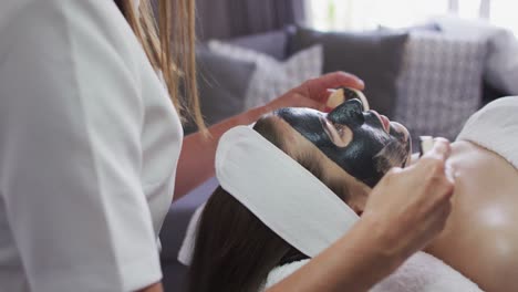 caucasian woman lying back while beautician gives her a face mask