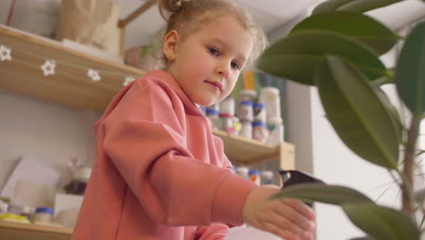 bottom view of a little girl spraying water on a plant at a table in a craft workshop