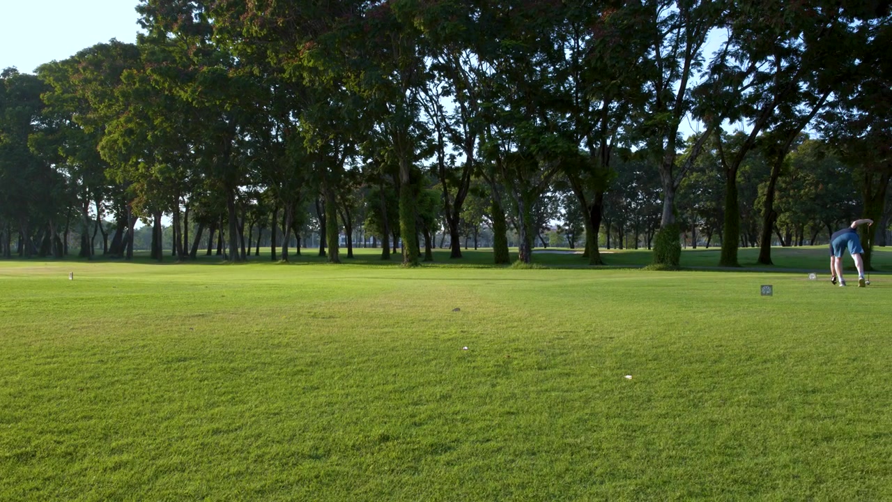 A man walks across a lush green golf course fairway under bright daylight conditions.