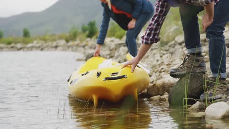 pareja caucásica pasando un buen rato en un viaje a las montañas, colocando un kayak en el agua