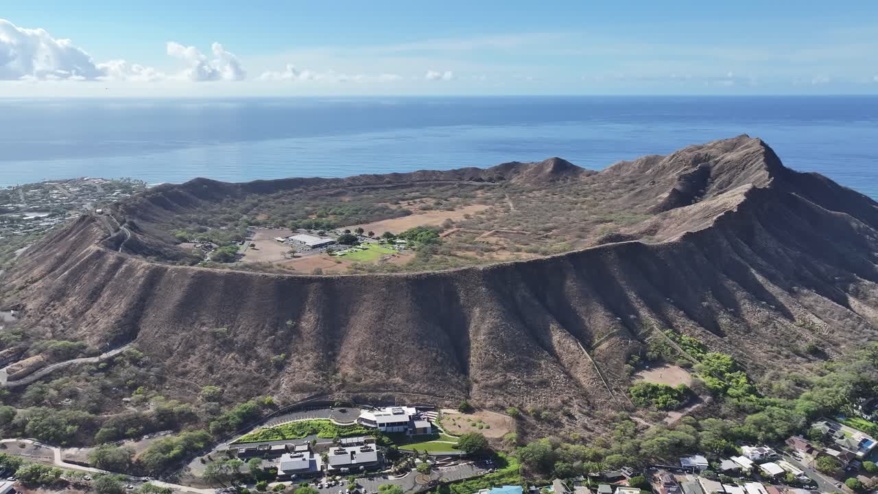 Aerial drone footage along the rim of Diamond Head volcanic crater on Oahu, Hawaii, showcasing panoramic tropical landscapes, turquoise ocean views, palm trees, and the scenic Waikiki coastline below
