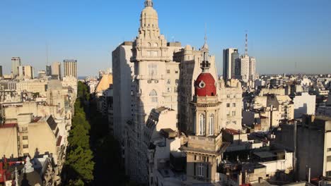 Aerial-dolly-out-of-Barolo-Palace-tower-and-Buenos-Aires-buildings-on-tree-lined-Avenida-de-Mayo-at-sunset