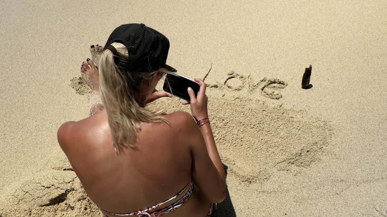 Sød ung pige tager billede af citat skrevet i strandsand, kærlighed er i luften