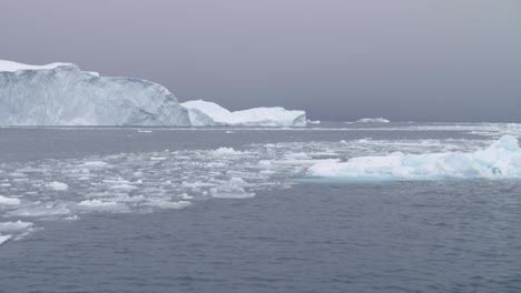 Slow-motion-pan-across-small-ice-floes-and-large-icebergs-floating-in-the-ocean-on-a-cloudy-day