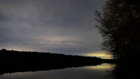 clouds moving over a lake at night as the stars move in the background