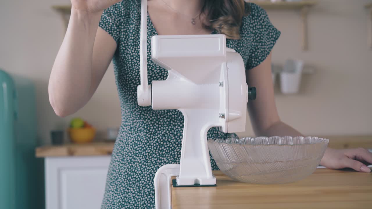 한 여자 가 테이블 클로즈업 에서 가정용 밀가루 분쇄기 의 손잡이 를 돌리고 있다