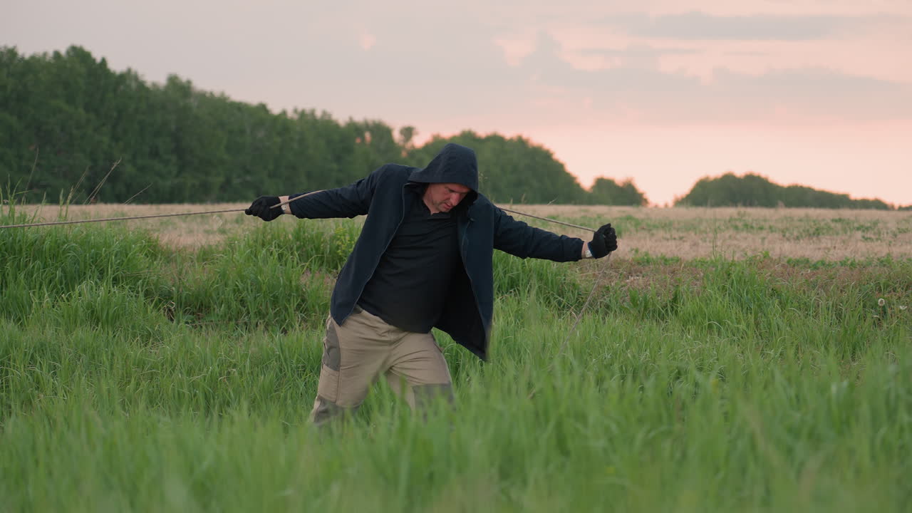 man in black hoodie pulling rope attached to deflated hot air balloon envelope across grassy open field at sunset in preparation for balloon pack up operation under cloudy sky at dusk
