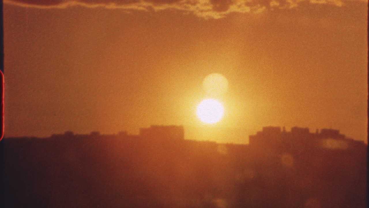 8 mm film - warm golden sunset illuminating urban skyline, vibrant orange hues spreading across cloudy sky during twilight transition