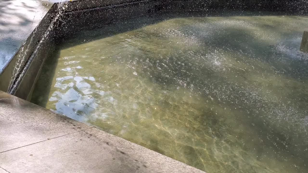 Marble fountain rim and rippled water surface with drops shining in sunlight