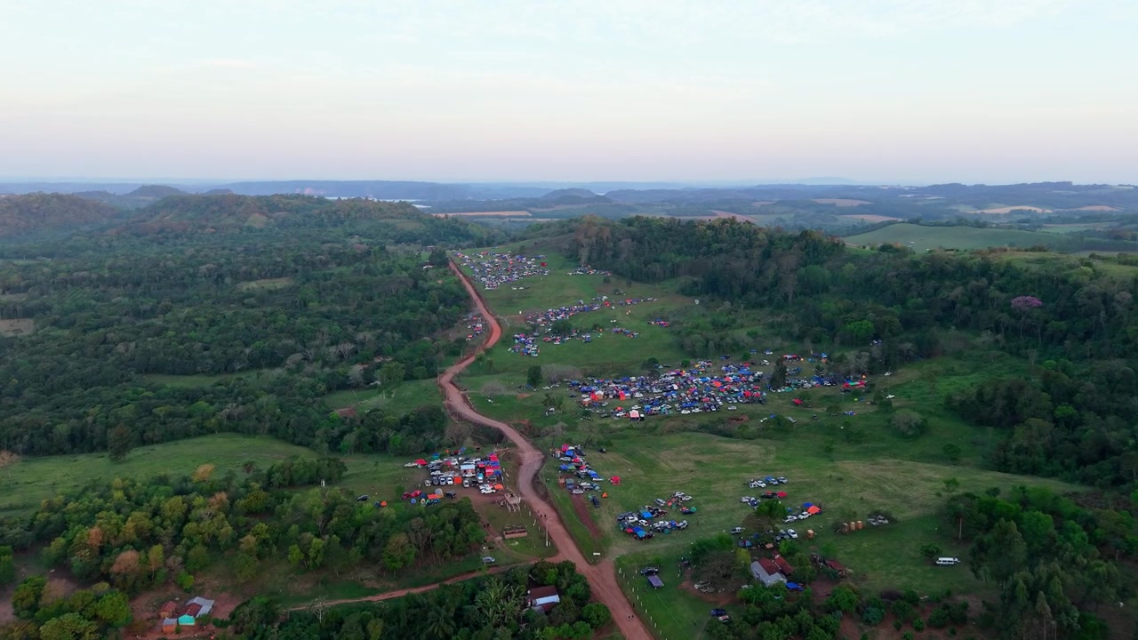Droneoptagelser viser en stor menneskemængde samlet langs en landlig grusvej til WRC Rally 2026 i Nueva Alborada, Paraguay. Farverige campingpladser og naturskønne skovklædte bakker