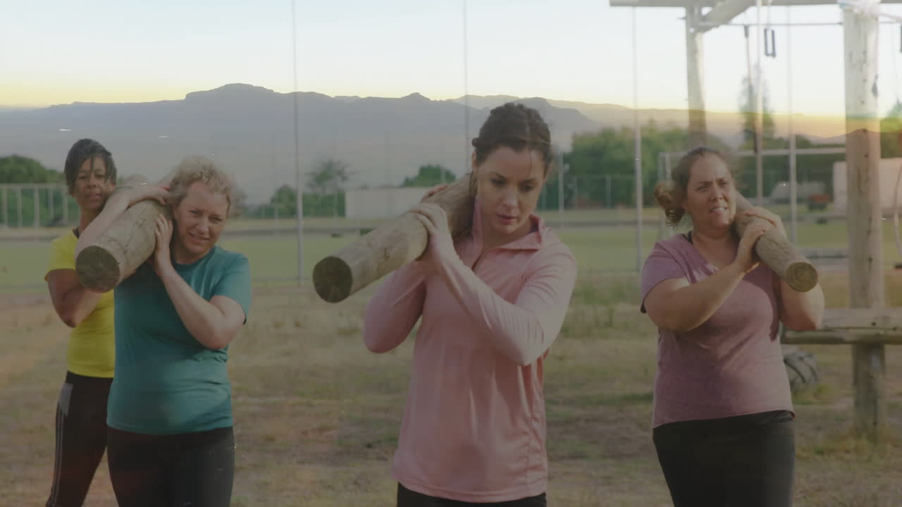 Carrying logs on shoulders, women doing outdoor fitness training session