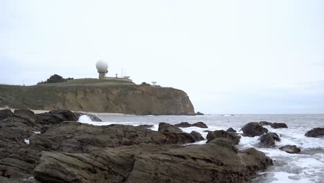 panoramic view of waves crashing onto rocks and the pillar point in the background