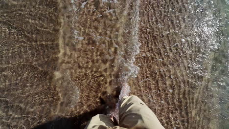 barefoot person walking on sandy sea coast with water, pov view