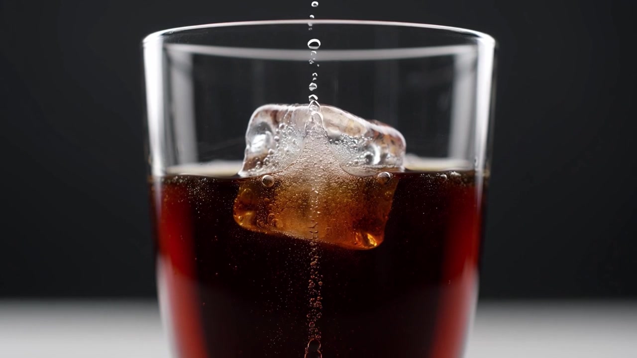 Liquido che si versa in un bicchiere con cubetti di ghiaccio.