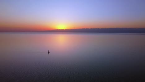 Drohnenaufnahmen-Aus-Der-Luft-Eines-Riesigen-Sees-Bei-Sonnenuntergang,-Die-Atemberaubenden-Farben-Und-Die-Beeindruckenden-Berge-Im-Hintergrund
