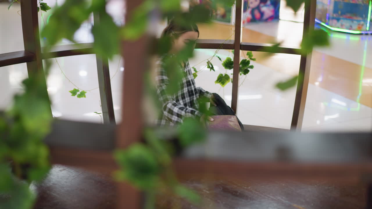 어린 소녀는 편안하고 장식된 공간에서 나무 테이블에 앉아 있으며, 진지한 표정으로 가방에서 물건을 꺼내며, 푸른색이 그 지역을 둘러싸고 평화롭고 집중된 분위기를 만니다.