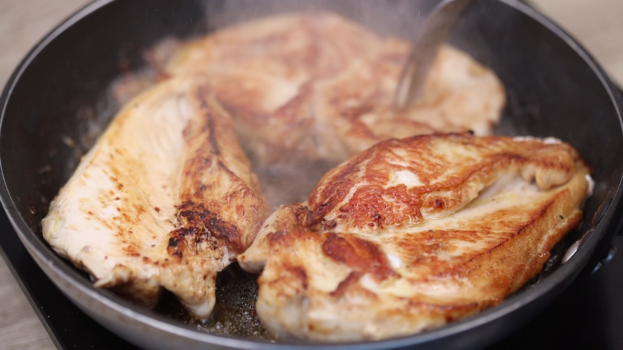 Close up of chicken breasts being flipped in hot pan revealing golden seared surface during cooking