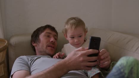 caucasian man looking smartphone with baby at home