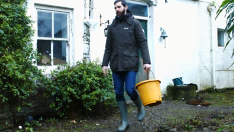 man walking out of door and carrying bucket of water