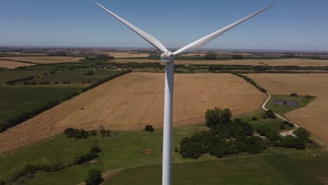 aerial close up shot of rotating wind turbine and agricultural fields in backdrop