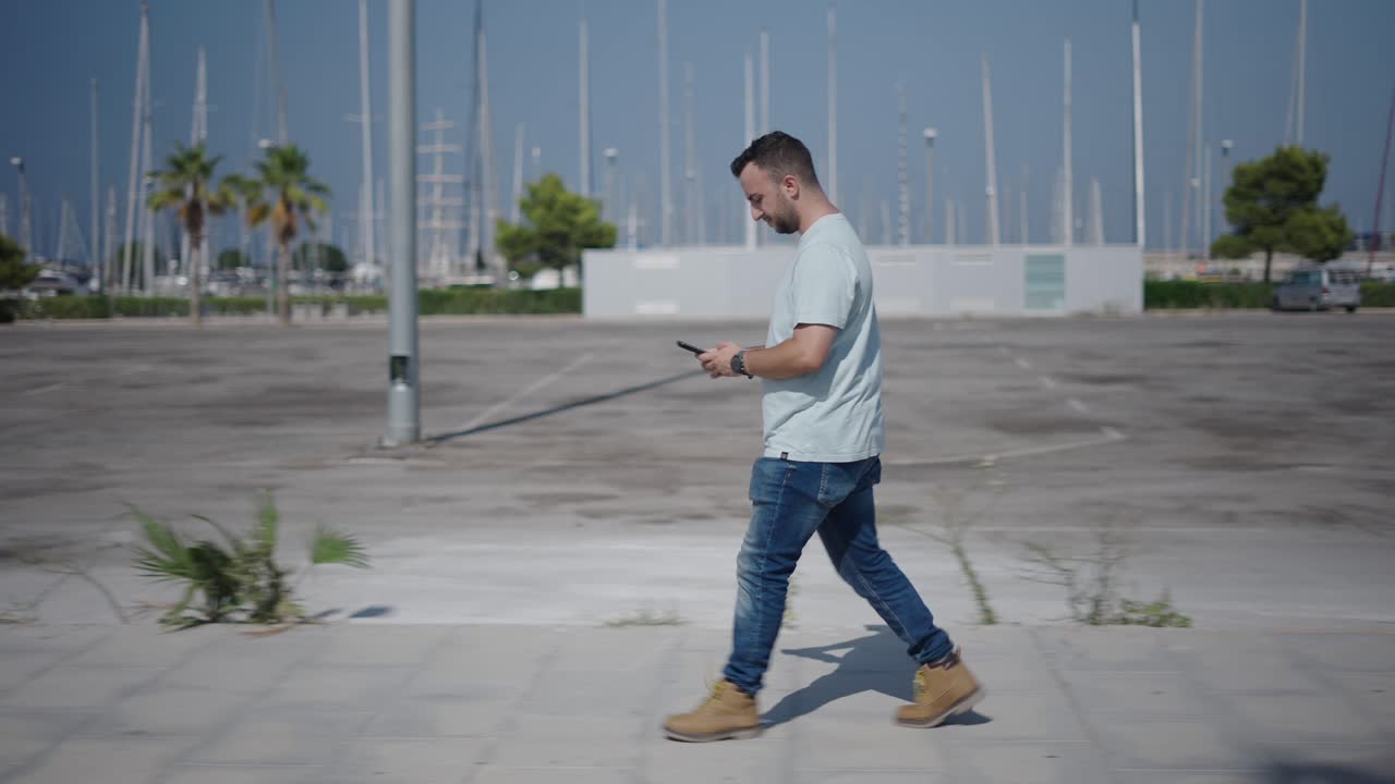 Man Walking and Using Phone at Waterfront Parking Lot