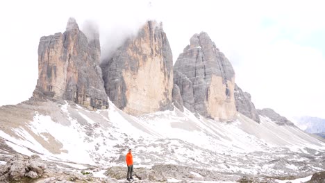 solo man jumps up in excitement at base of dolomiti with snowy tre cime di lavaredo behind