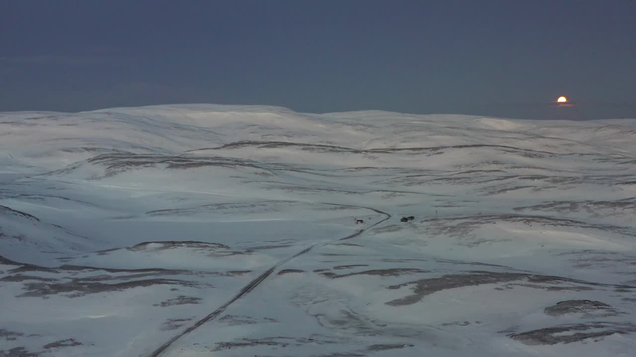 The road towards the most northern part of Europe, Nordkapp, during winter, with in the background a full moon. Aerial shot going backwards.