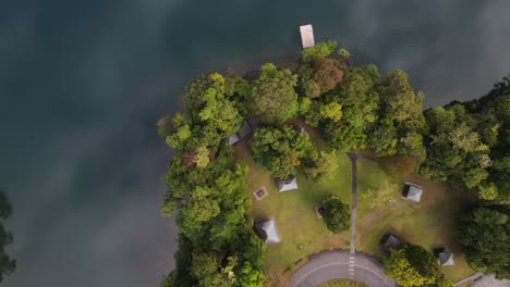 Statisches-Drohnenvideo-Mit-Blick-Auf-Einen-üppigen-Parkbereich-Neben-Einem-Vulkanischen-Kratersee-Mit-Wolken,-Die-Sich-Im-Ruhigen-Wasser-Spiegeln