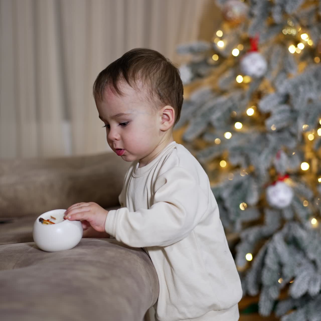 Adorable Caucasian kid playing with a toy in the room. Black cat appears from behind the Christmas tree