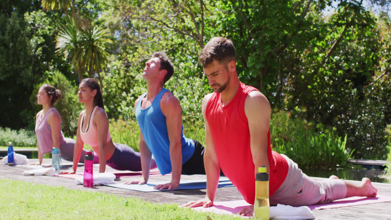 grupo diverso de hombres y mujeres practicando yoga estirándose en esteras en un parque soleado