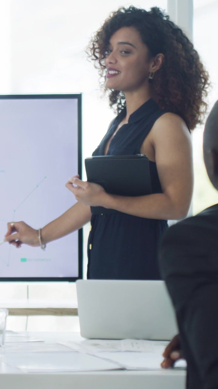 Donna d'affari che presenta grafici di dati ai colleghi durante una riunione in ufficio